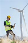 Worker using laptop by wind turbine in rural landscape