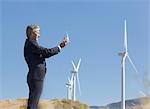 Businessman with glass of water by wind turbines in rural landscape