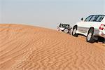 Sports utility vehicles driving up desert sand dune
