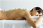 Woman lying on massage table, flowers lined up on her back