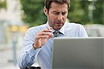 Businessman smoking while using laptop computer outdoors