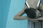 Woman lying on deck next to pool, resting head on arms