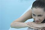 Woman lying next to pool, resting head on arms, looking away