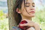 Woman relaxing outdoors with eyes closed, holding apple