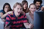 Young man playing video games while friends watch with astonishment