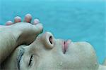 Young man touching forehead with back of hand, eyes closed, water in background