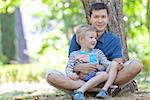 handsome smiling father and his cute son sitting together in the woods