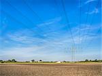 Power cable and power pole over a field under a blue sky with white clouds