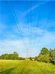 Power cable and power pole on a green meadow under a blue sky with white clouds