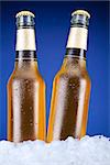 Two beer bottles sitting on ice over a blue background.