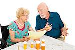 Senior couple at the dining room table discussing medical and prescription costs.  White background.