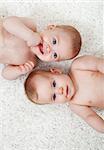 Twin babies laying on the floor smiling and curious