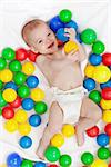 Happy baby boy in diapers with lots of colorful balls playing