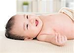 Adorable six months old Asian baby girl lying on bed smiling.