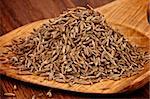 Heap of Cumin Seeds in Wooden Spoon closeup on Wooden background