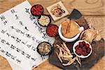 Traditional chinese herbal medicine selection with mandarin calligraphy on rice paper over oak. Translation describes the medicinal functions to increase the bodys ability to maintain body and spirit health and balance energy.