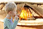 cheerful little boy eating smores by fire