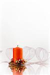 Christmas candle decoration with orange, flasks and white ribbon on a shiny surface