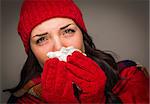 Sick Mixed Race Woman Wearing Winter Hat and Gloves Blowing Her Sore Nose with a Tissue.