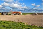 tractor plowing field in spring by Dutch farmhouse