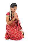Indian girl in a greeting pose, traditional sari costume, full length kneeling on floor isolated on white background