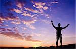 Silhouette of businessman standing on top mountain open arms looking at the sunrise or sunset