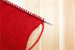 Stockinette stitch in red wool on a knitting needle, on wooden background