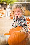 Adorable Little Boy Smiles While Leaning on a Pumpkin at a Pumpkin Patch in a Rustic Setting.