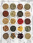 Herb tea selection in white porcelain dishes over distressed wooden background.