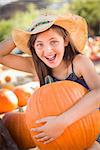 Preteen Girl Holding A Large Pumpkin at the Pumpkin Patch in a Rustic Setting.