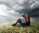 Tourist resting on the hill under storm clouds