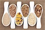 Healthy breakfast cereal selection in white porcelain scoops over hessian background.