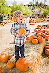 Adorable Little Boy Sitting and Holding His Pumpkin in a Rustic Ranch Setting at the Pumpkin Patch.