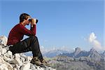 Young man looking through binoculars in the mountains