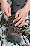 Tying the hiking boots of a hiker on a rock in the mountains