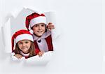 Happy kids in santa outfits looking through hole in paper - christmas joy concept, with copy space