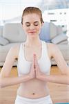 Toned young woman sitting in Namaste position with eyes closed at fitness studio