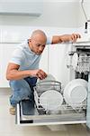 Serious young man using dish washer in the kitchen at home