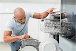 Serious young man using dish washer in the kitchen at home