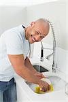 Portrait of a smiling young man doing the dishes at kitchen sink in the house