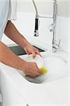 Close up mid section of a man doing the dishes at kitchen sink in the house