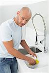 Portrait of a young man doing the dishes at kitchen sink in the house