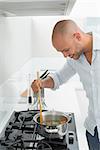 Side view of a smiling young man preparing food in the kitchen at home