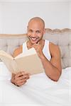 Portrait of a smiling relaxed young bald man reading book in bed at house