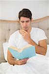 Relaxed young man reading book in bed at house