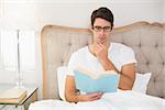 Relaxed young man reading book in bed at house