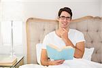 Portrait of a relaxed young man reading book in bed at house