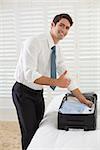 Side view portrait of a smiling businessman unpacking luggage at a hotel bedroom
