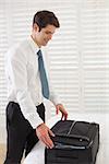 Side view of a smiling businessman unpacking luggage at a hotel bedroom