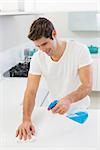 Smiling young man cleaning kitchen counter in the house